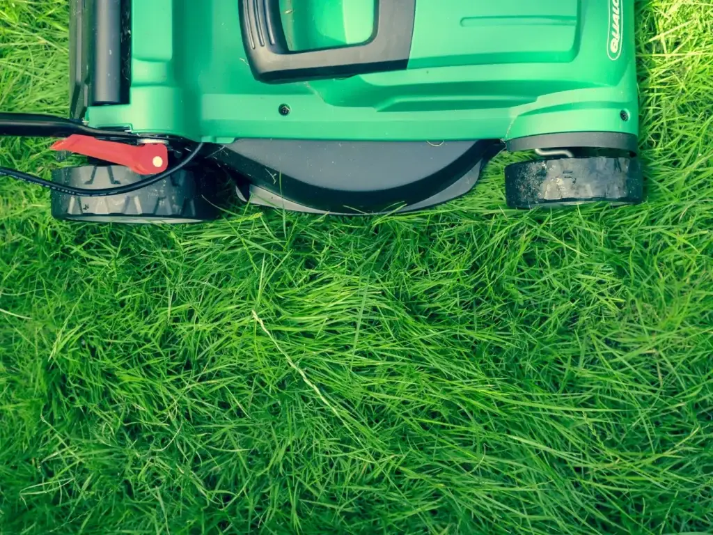 Close-up of a bright green electric lawn mower trimming fresh grass — showcasing professional garden maintenance and lawn care services by Reshape Landscaping Dubai.