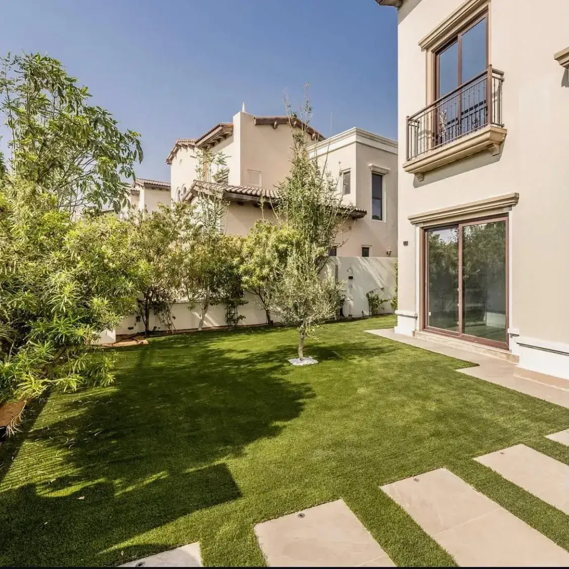Modern villa garden in Dubai featuring a vibrant artificial lawn, framed by light stone paving, Mediterranean-style architecture, and mature olive trees — a bespoke low-maintenance garden created by Reshape Landscaping Dubai.
